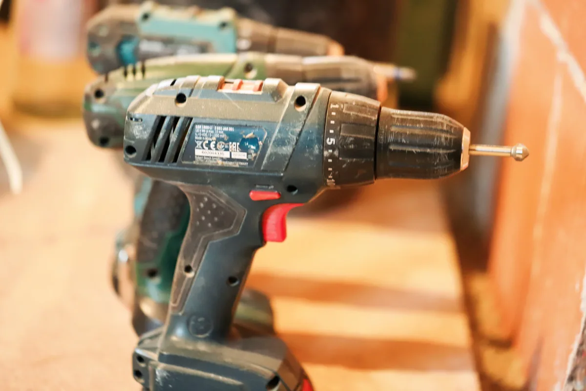 A row of cordless power drills on a wooden workbench