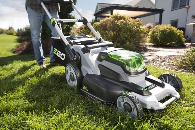 Homeowner using cordless battery-powered lawn mower on residential yard